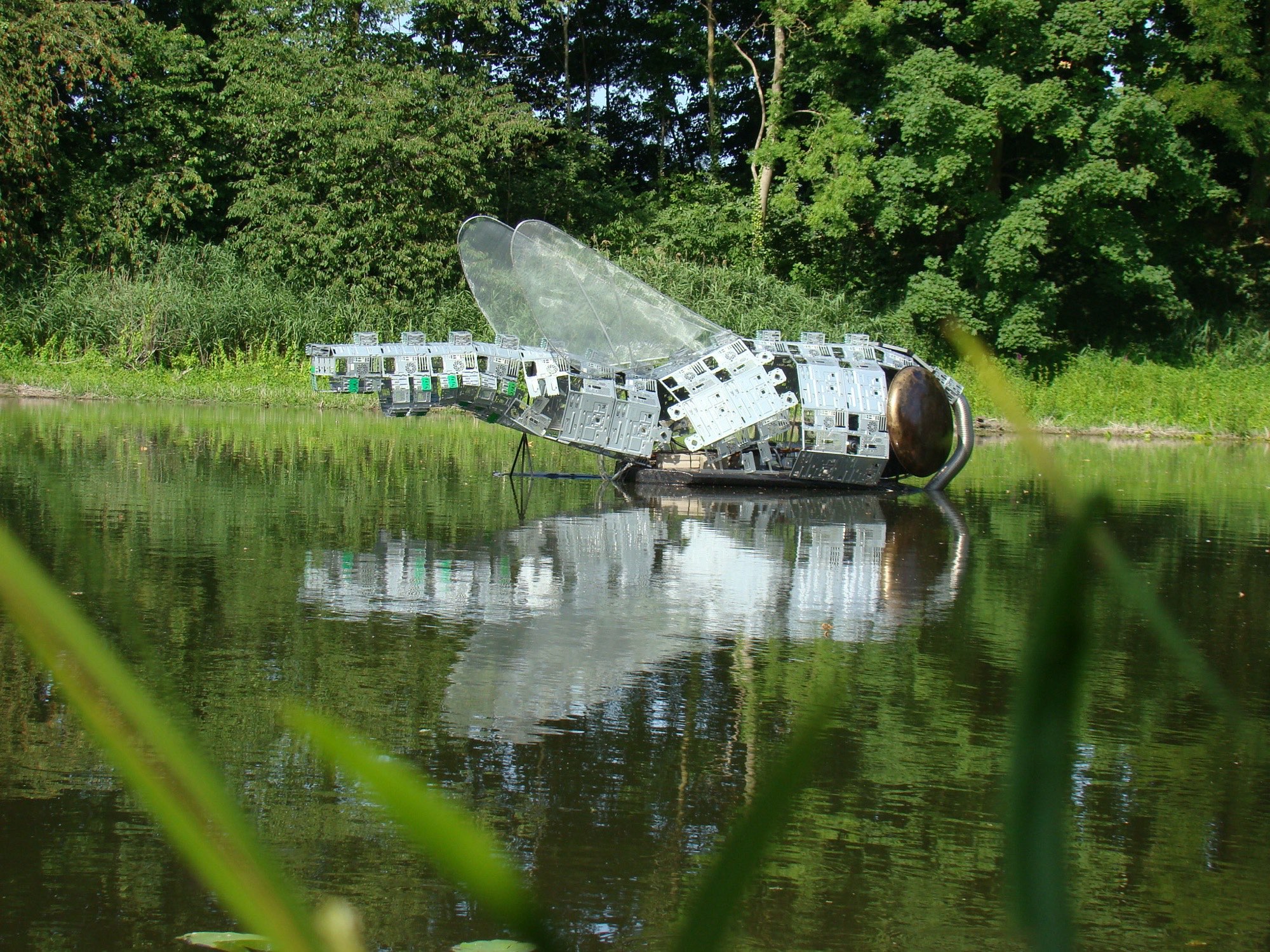 Libelvormig kunstwerk dat weerspiegelt in het water van de gracht