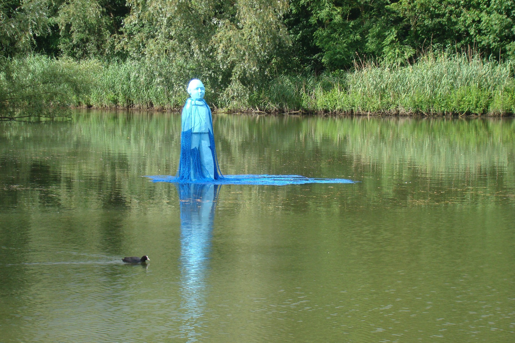 Blauw figuratief kunstwerk dat in de gracht staat, met spiegeling in het water